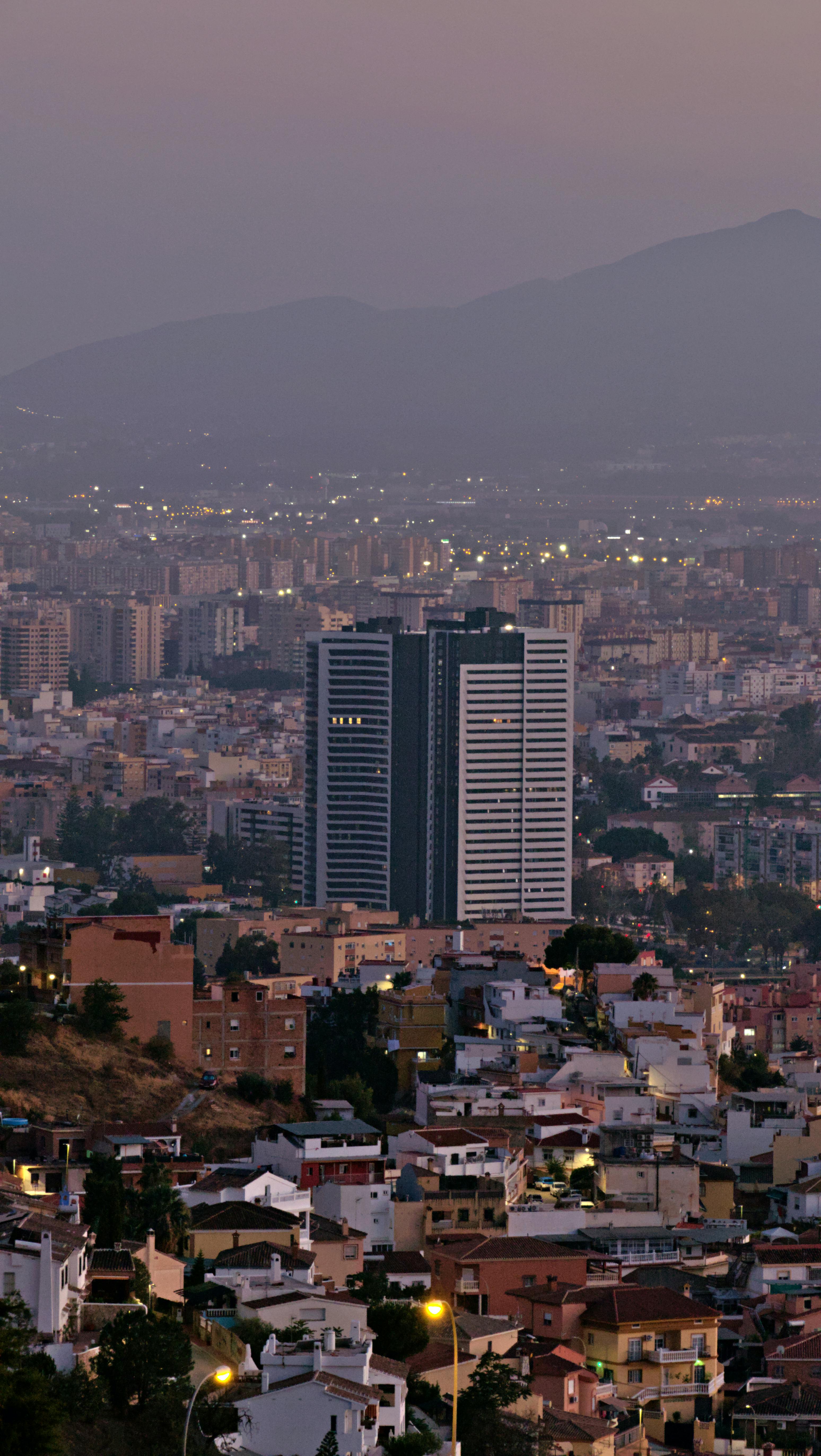 a city at dusk with buildings and mountains in the background