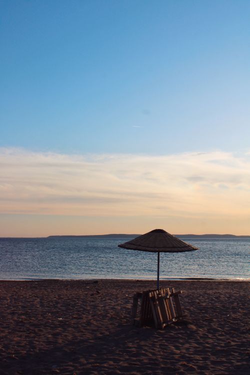 Free Peaceful beach view with a straw umbrella silhouetted against a colorful sunset sky. Stock Photo