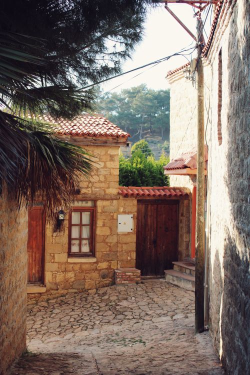 Free Quaint stone alley with rustic architecture and orange-tiled roofs, bathed in sunlight for a warm, traditional feel. Stock Photo