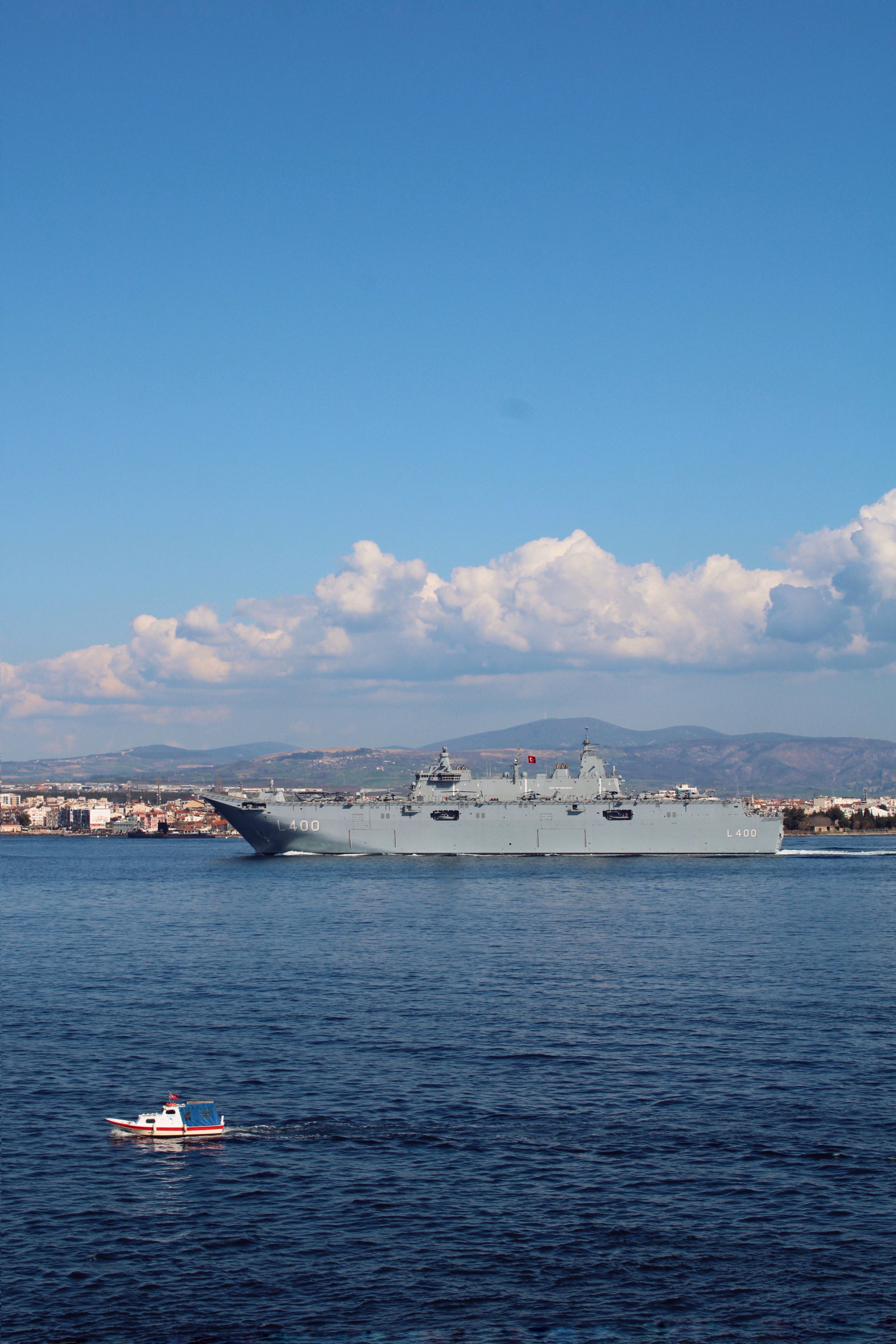 A large military ship sails near a small boat in a peaceful ocean setting under a clear blue sky.