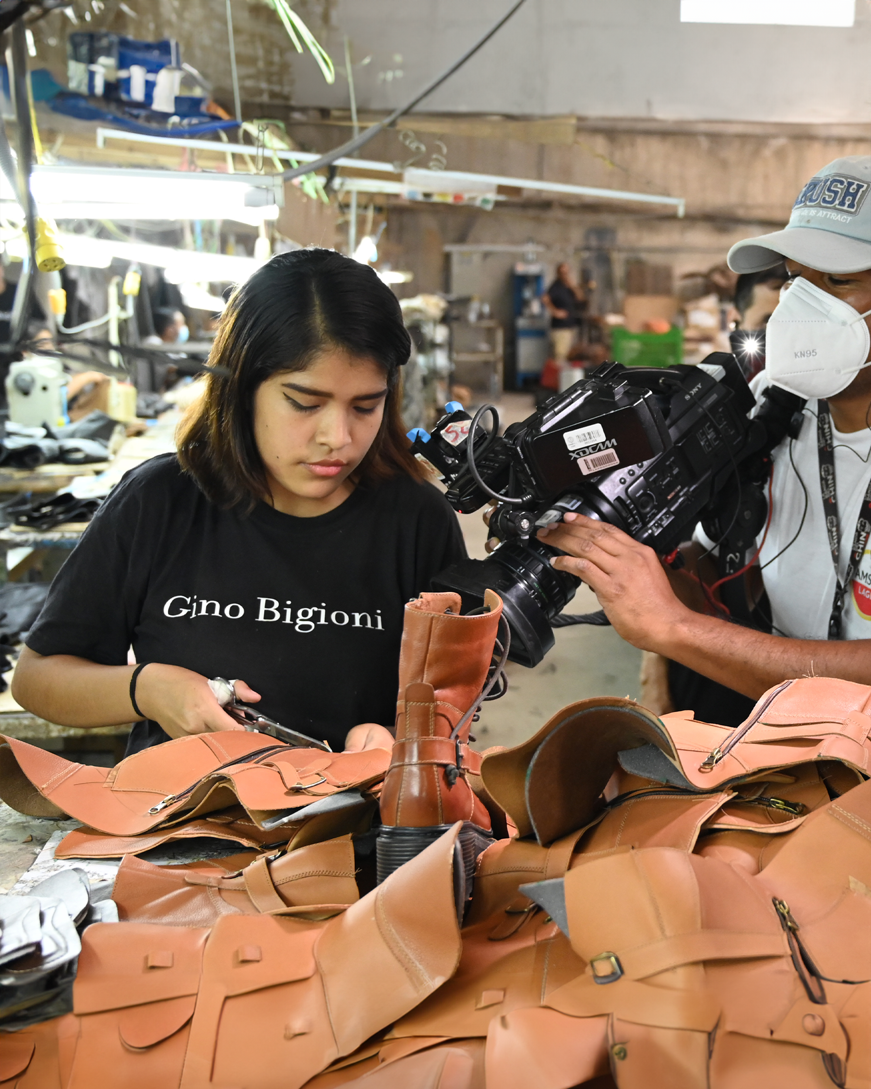 A woman crafts leather goods while being filmed in an artisan workshop.