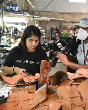 A woman crafts leather goods while being filmed in an artisan workshop.