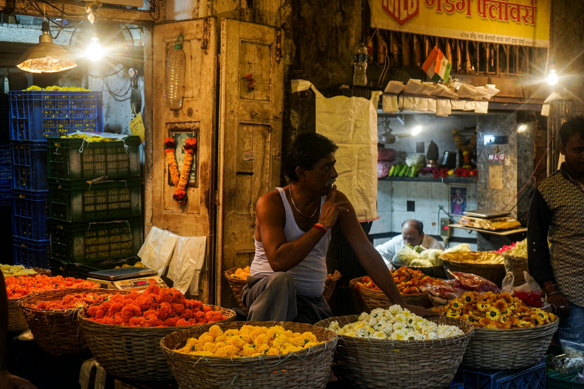 A bustling flower market in India with vendors and colorful flower baskets under warm lighting.