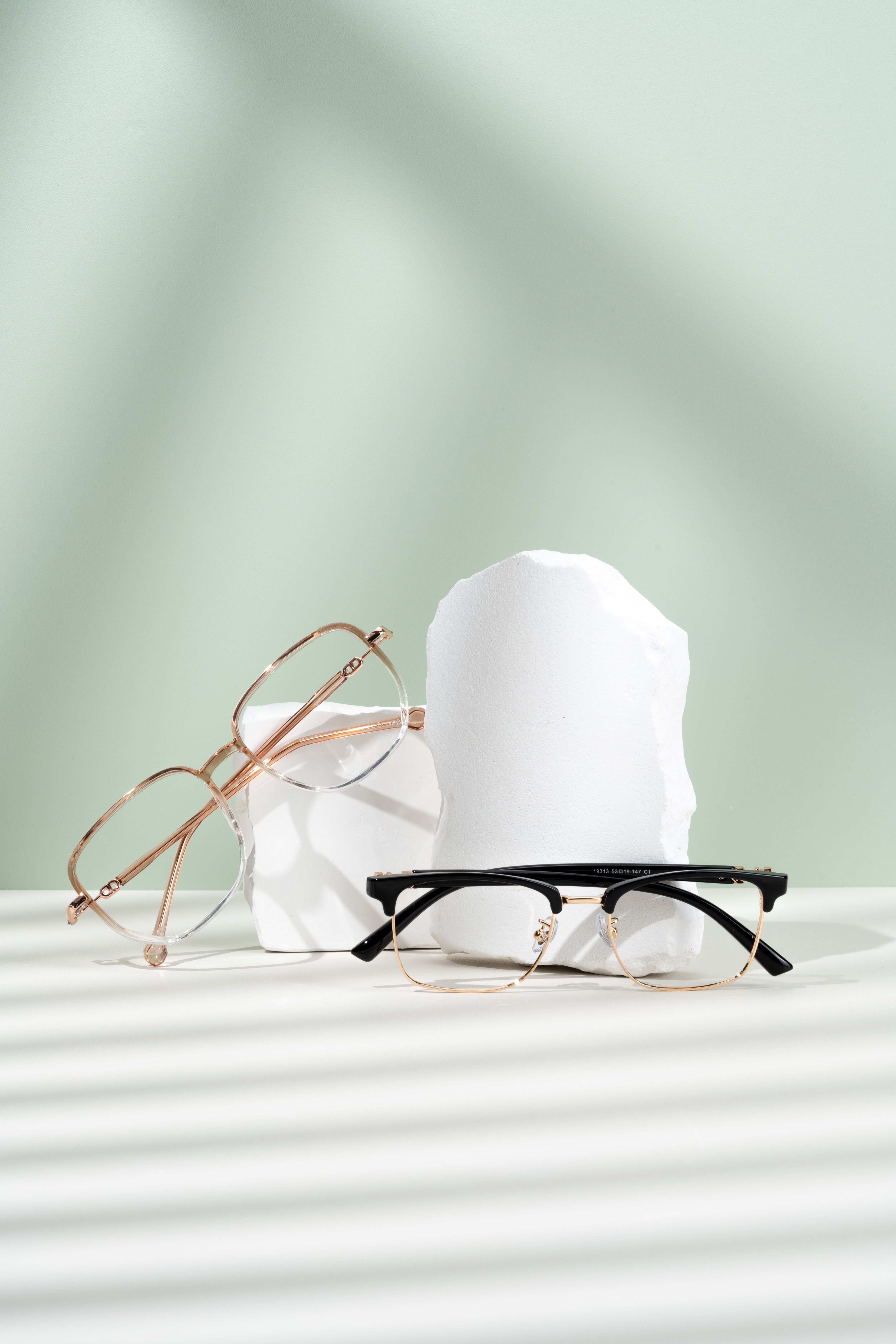 Stylish eyeglasses on a minimalist display with shadows and a mint background.