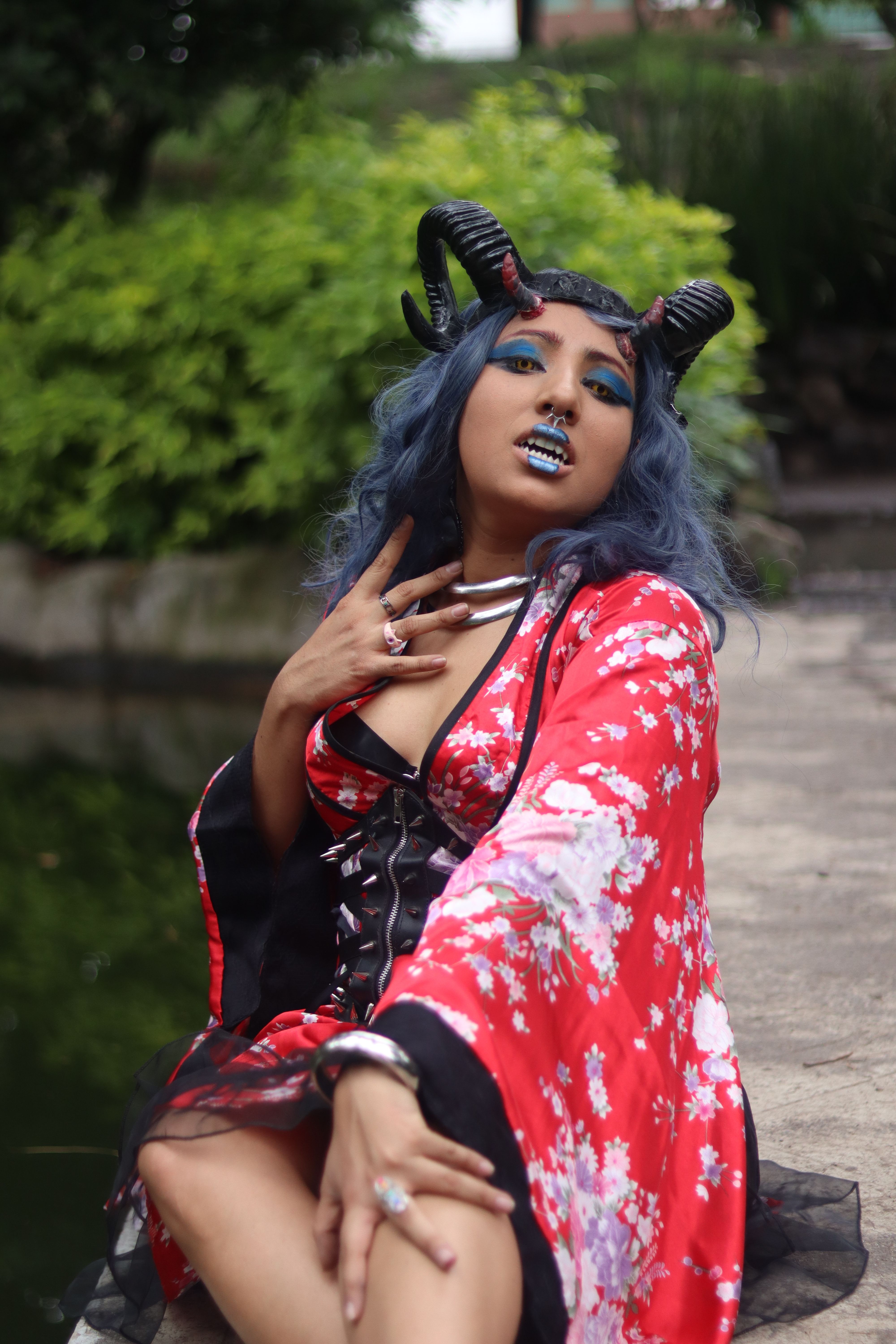 Capture of a woman in cosplay with vibrant makeup and horns in a garden setting.