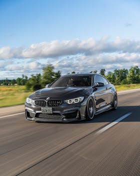 A sleek BMW M4 speeds down an open highway under clear skies, showcasing automotive design and performance.