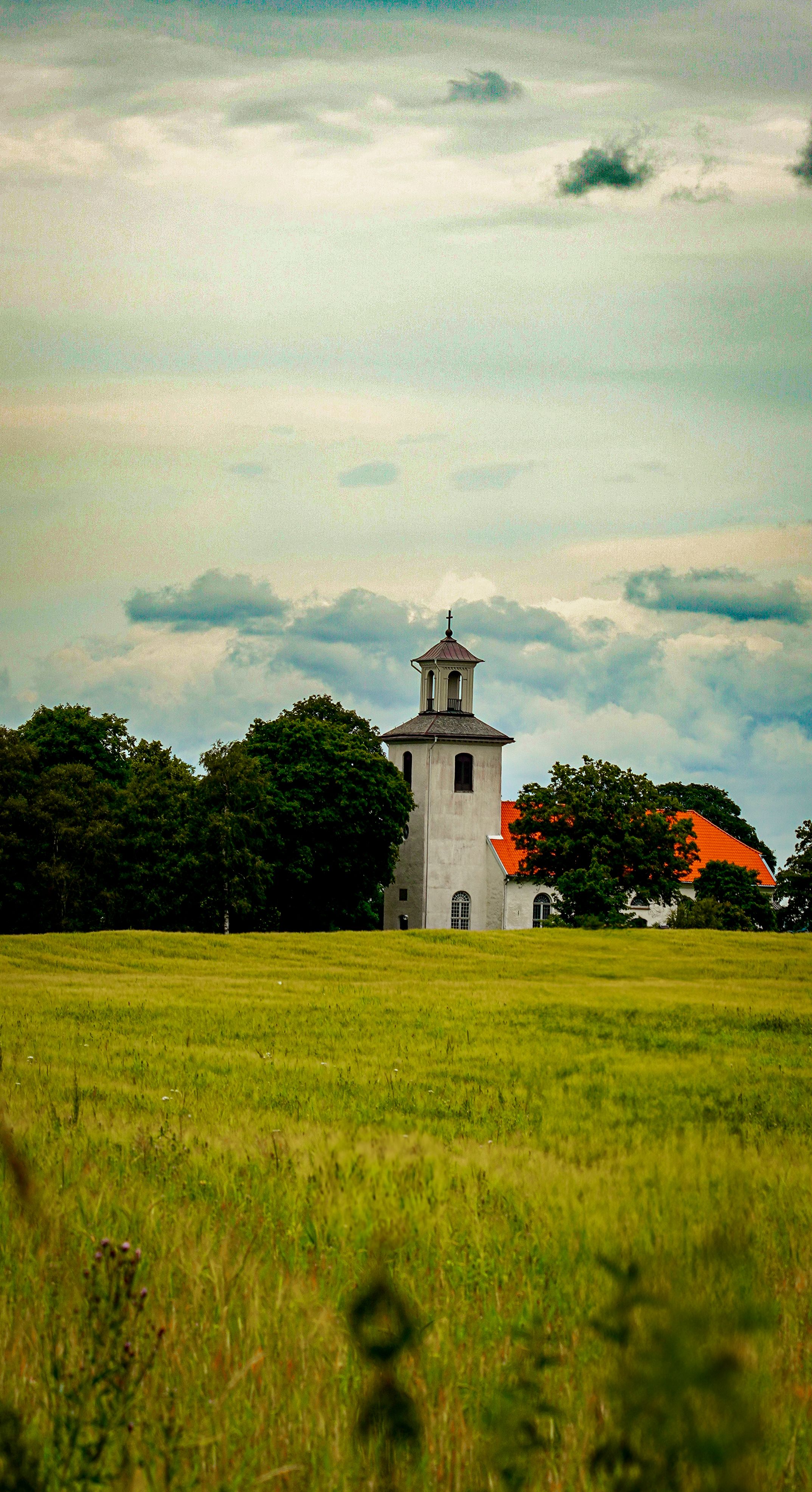 Charming church tower standing in a lush green field under a cloudy sky.