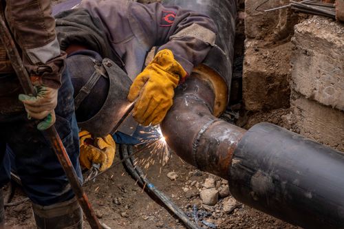 Technician welding a steel pipe outdoors during a full home repiping project