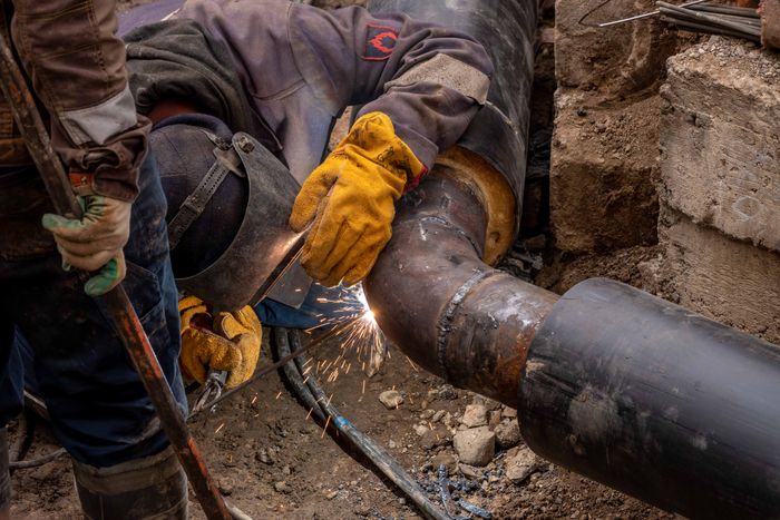 Welder joining a steel pipe outdoors at a facility