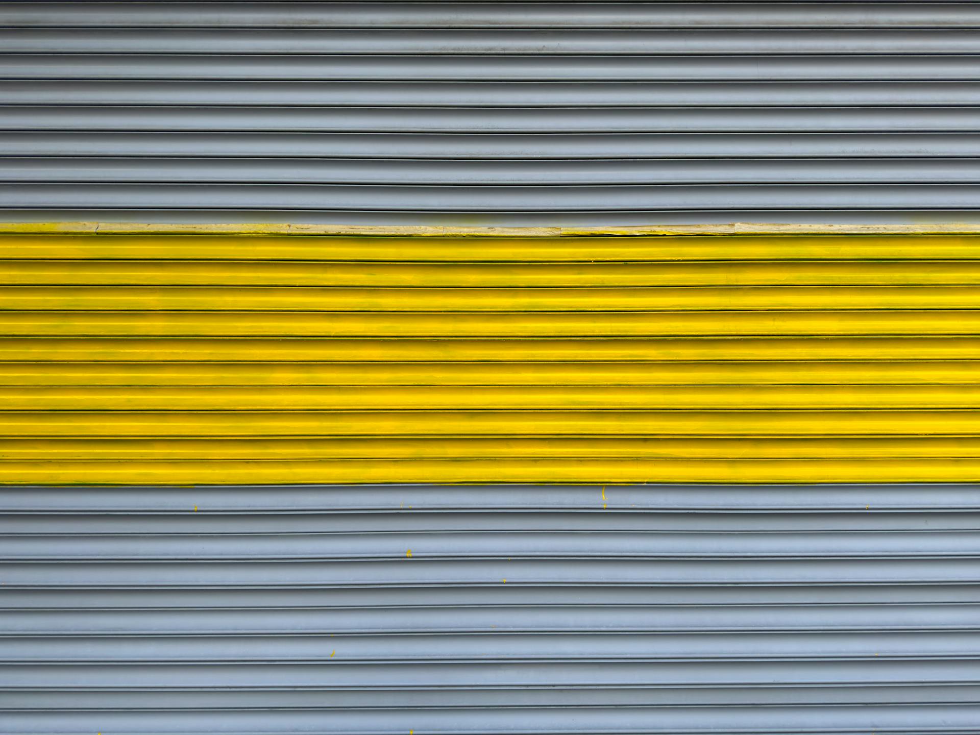 Close-up of a metal shutter featuring yellow and grey stripes, displaying a modern and minimalist design.