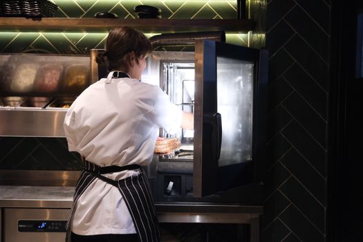 A chef in a striped apron prepares food using a commercial kitchen oven.