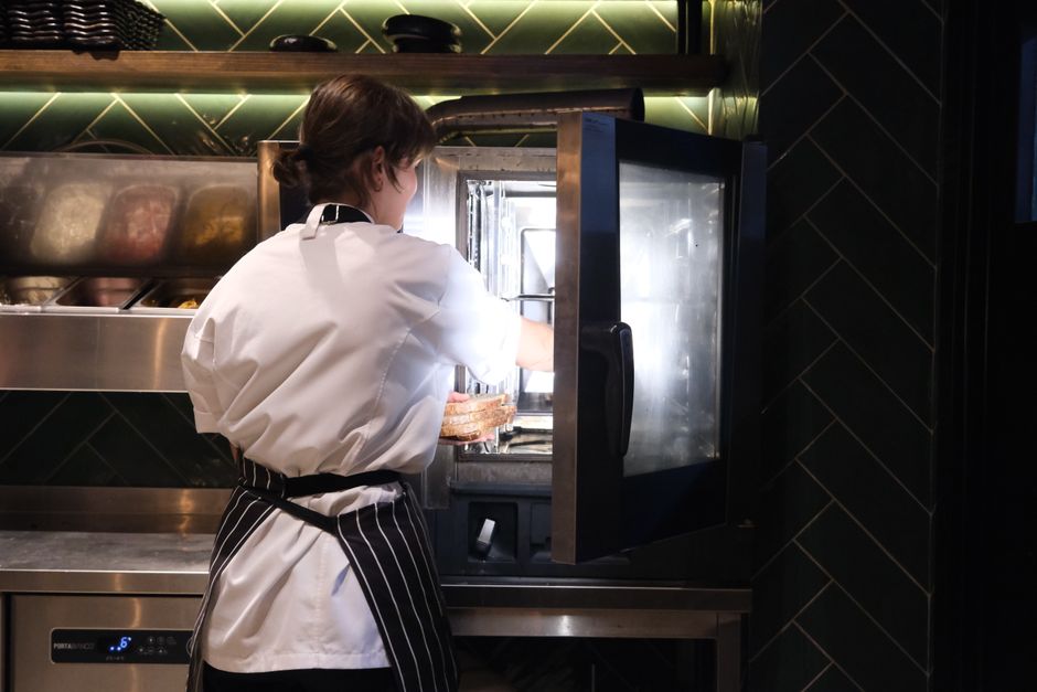 A chef in a striped apron prepares food using a commercial kitchen oven.