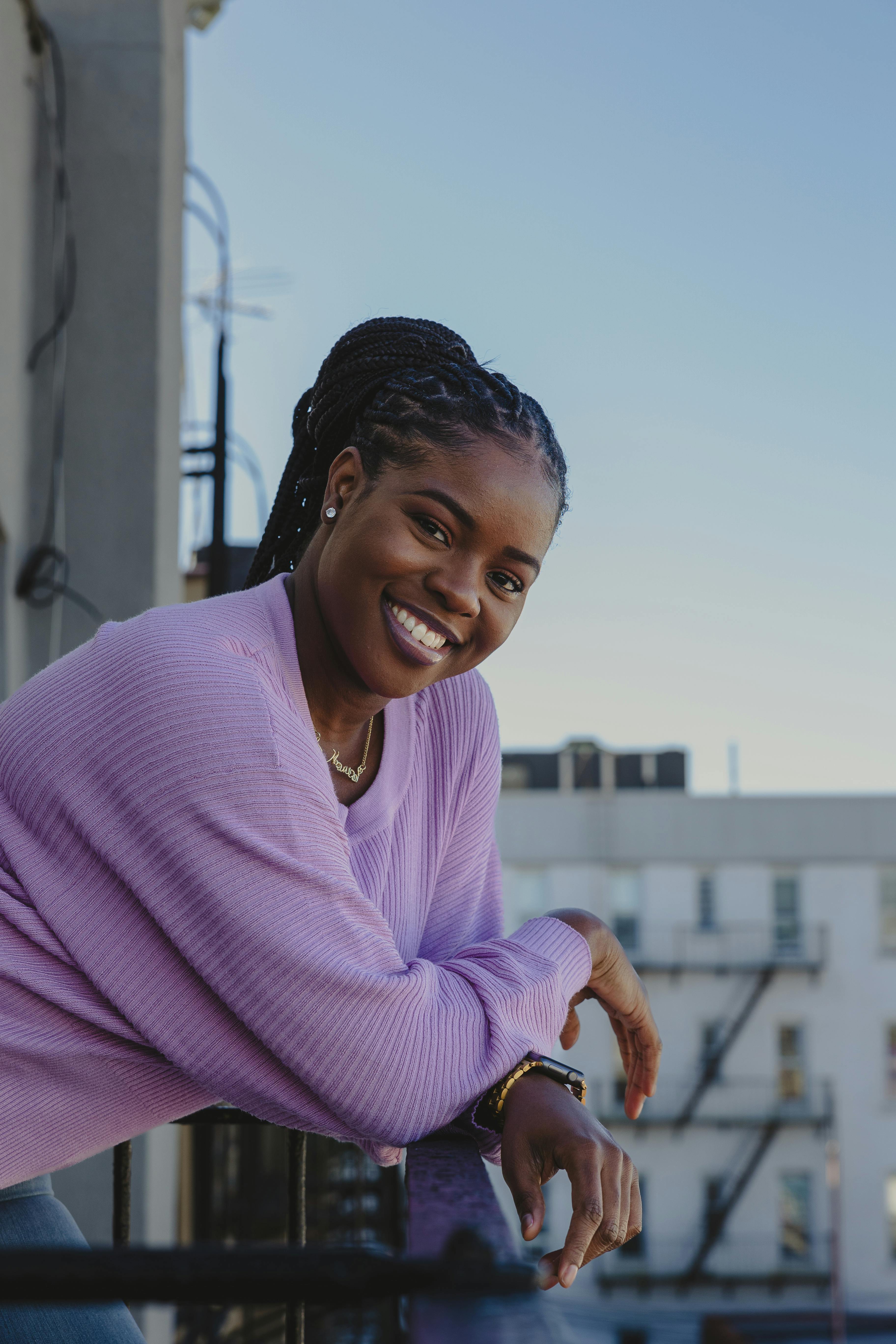 Cheerful woman in a purple sweater enjoying a sunset on a New York City balcony.