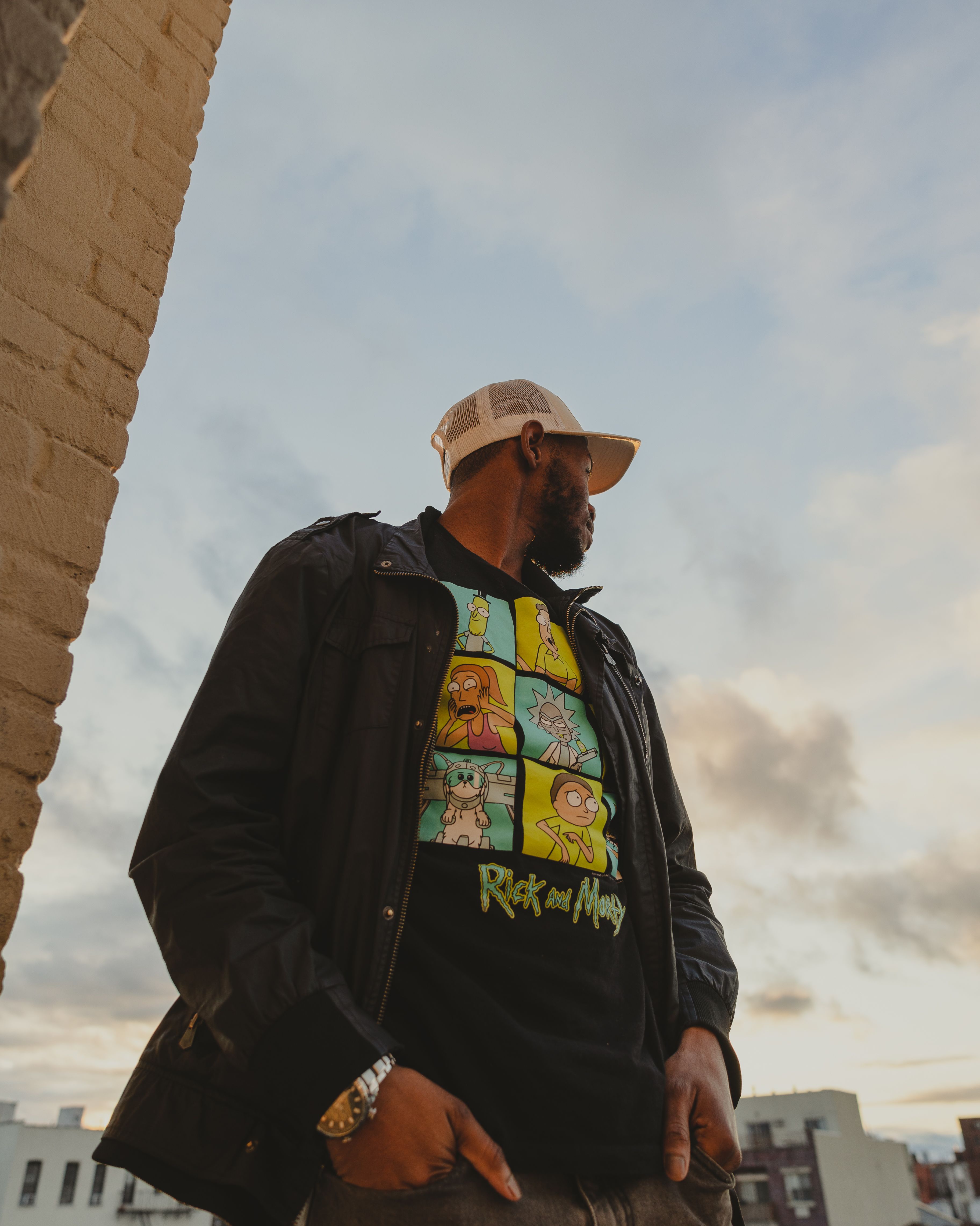 A man standing outdoors in New York City, wearing a cap and graphic t-shirt during sunset.