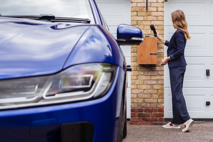 A person using a wall-mounted home EV charging station next to a blue electric car on a driveway