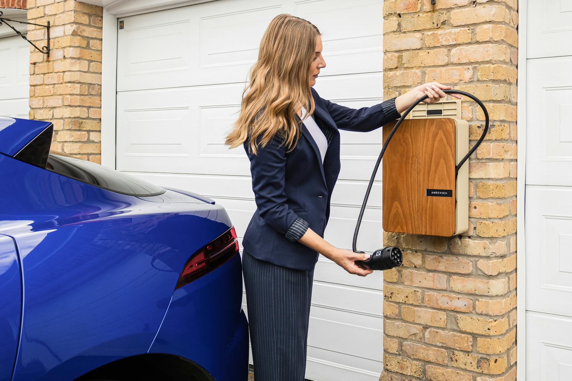 Young woman unwinding a bespoke Andersen home EV charge point to charge a fully electric Jaguar I-Pace