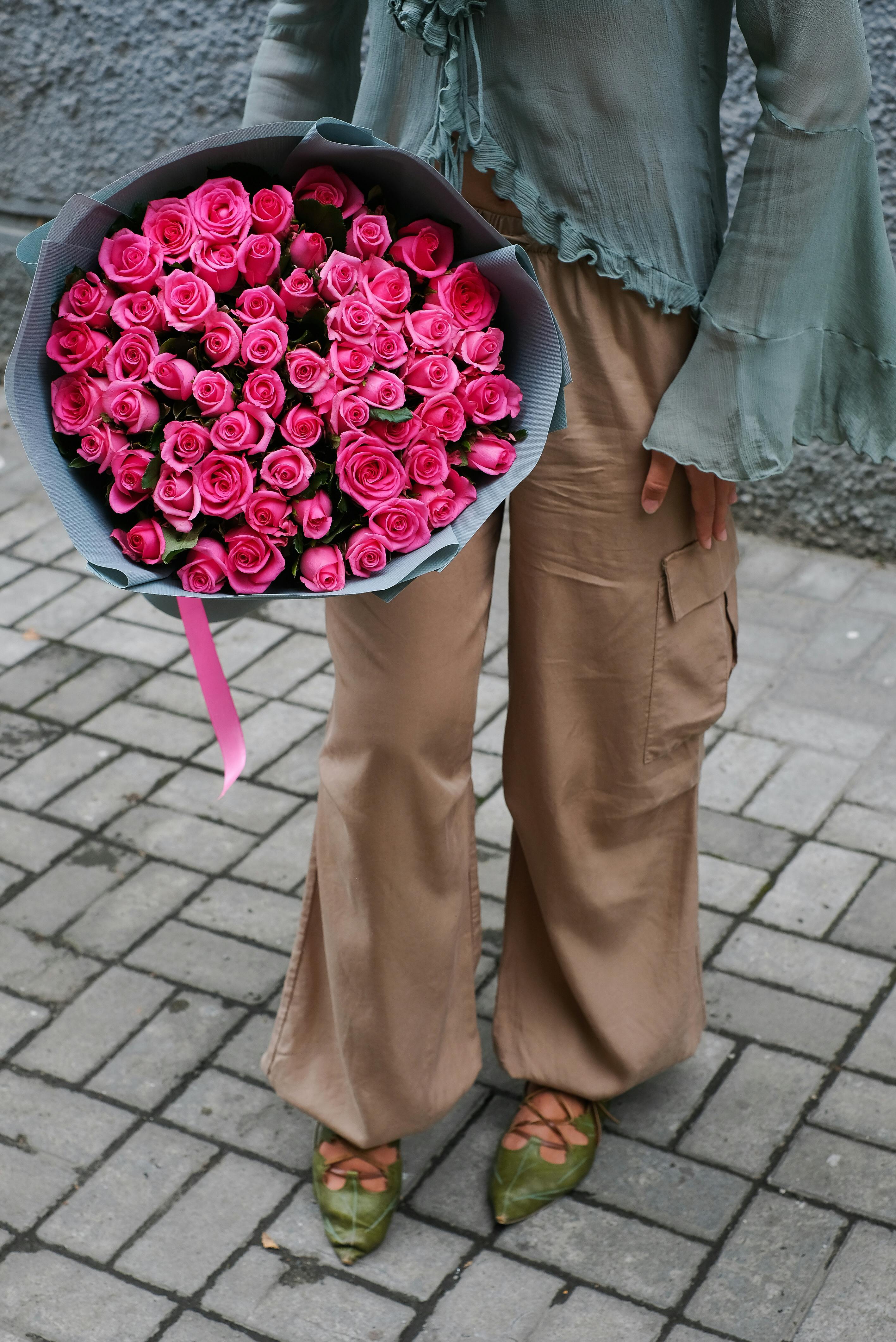 A stylish woman holds a vibrant bouquet of pink roses outdoors.