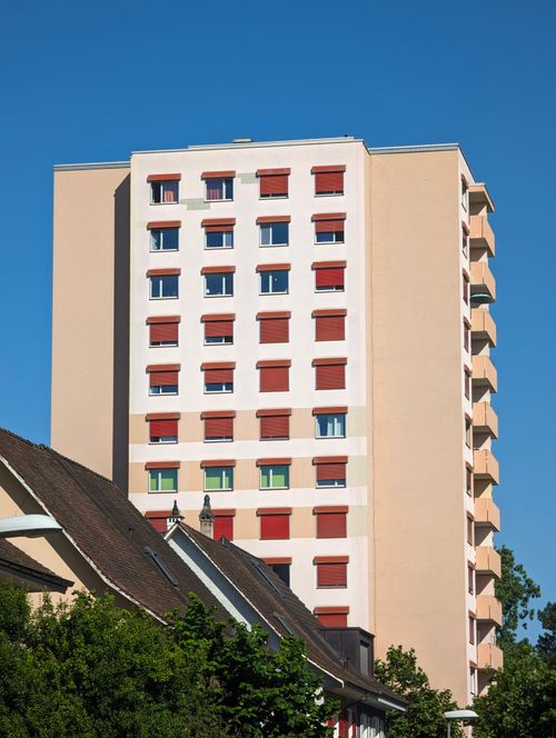 Free A contemporary apartment building with red window shutters against a clear blue sky. Stock Photo