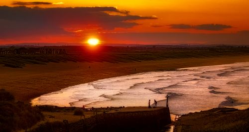 Free Beautiful sunset over a quiet beach with gentle waves and silhouettes of people on the shore. Stock Photo