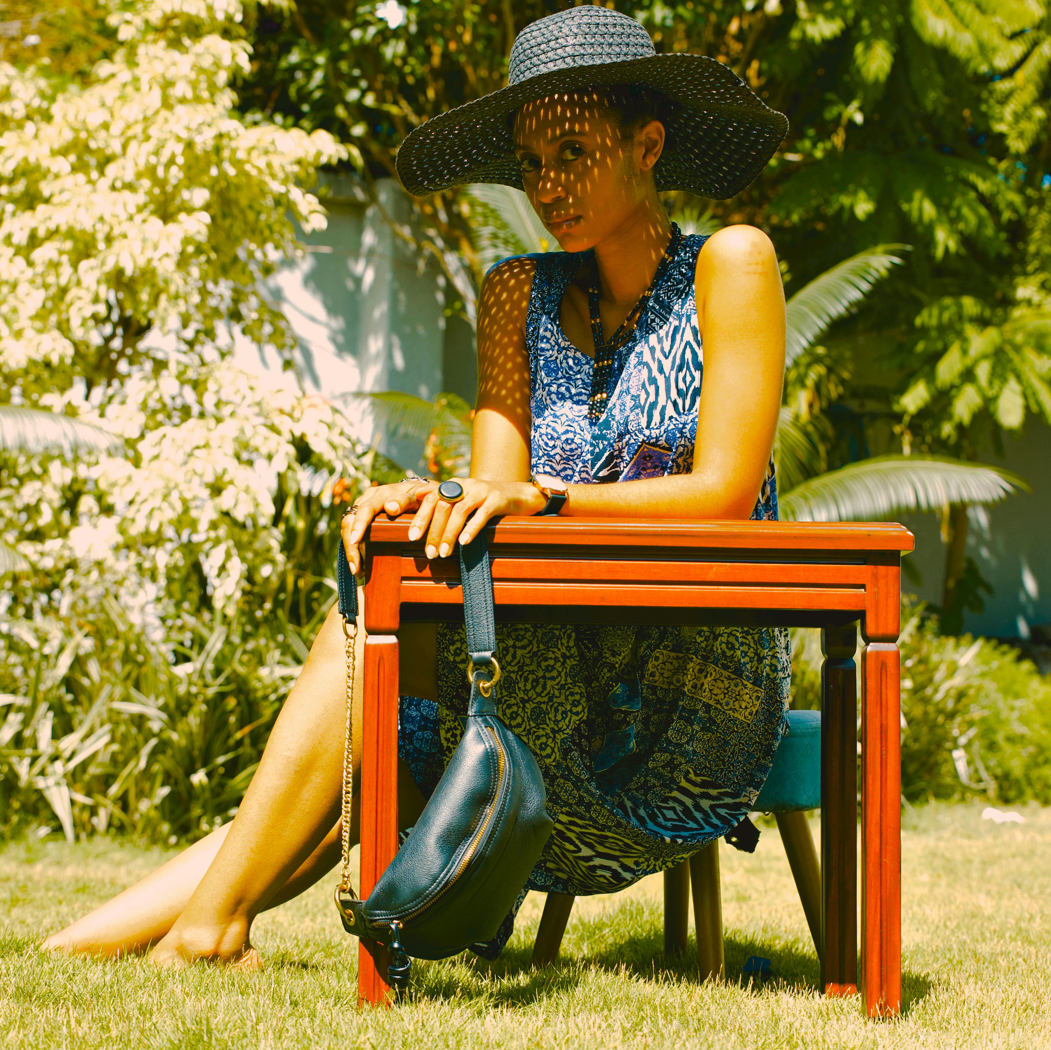 Woman in summer dress sitting outdoors with a hat and handbag, enjoying the sunny weather.