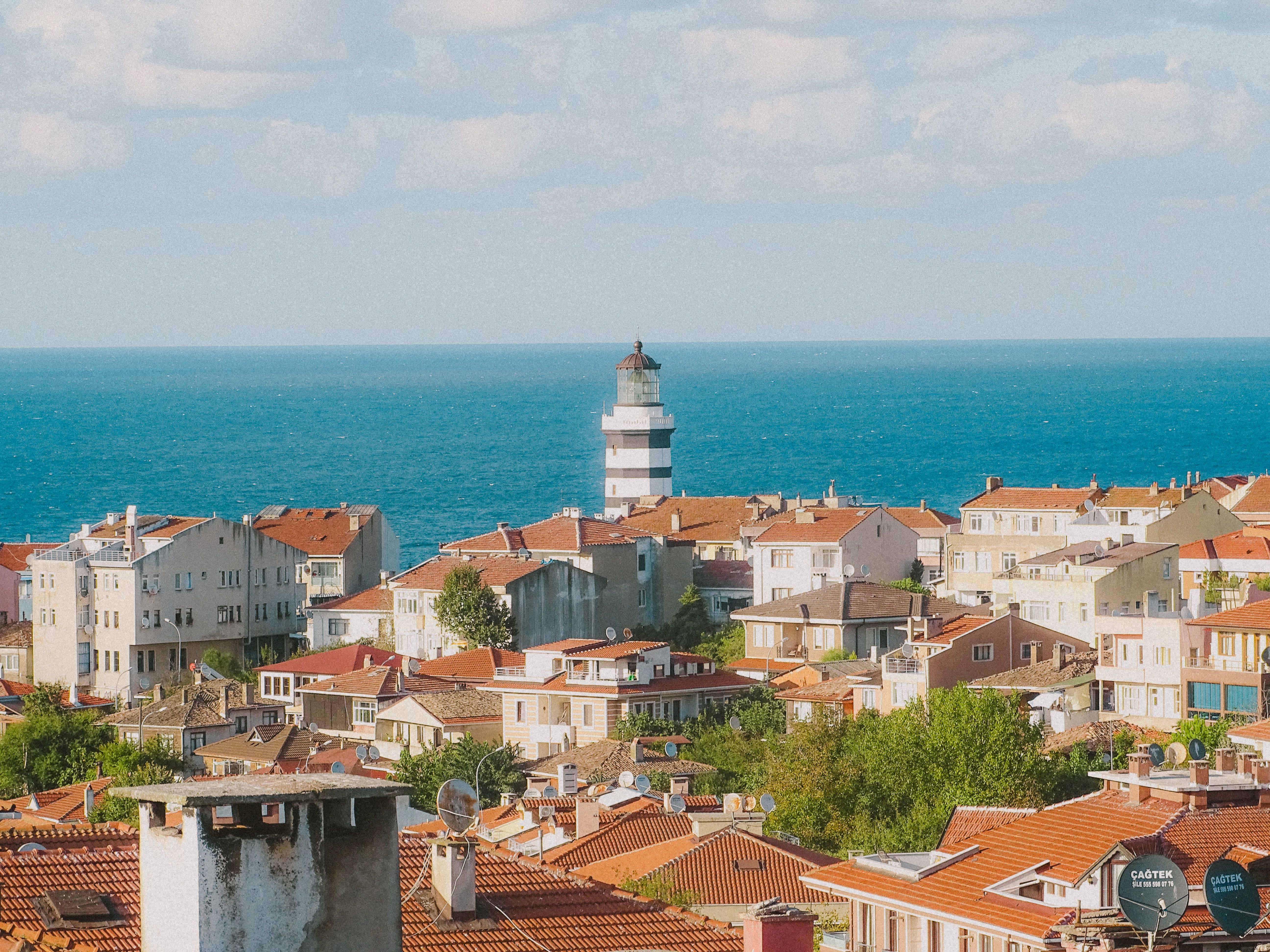 Scenic view of a coastal town with a lighthouse by the ocean, perfect for summer vacation vibes.