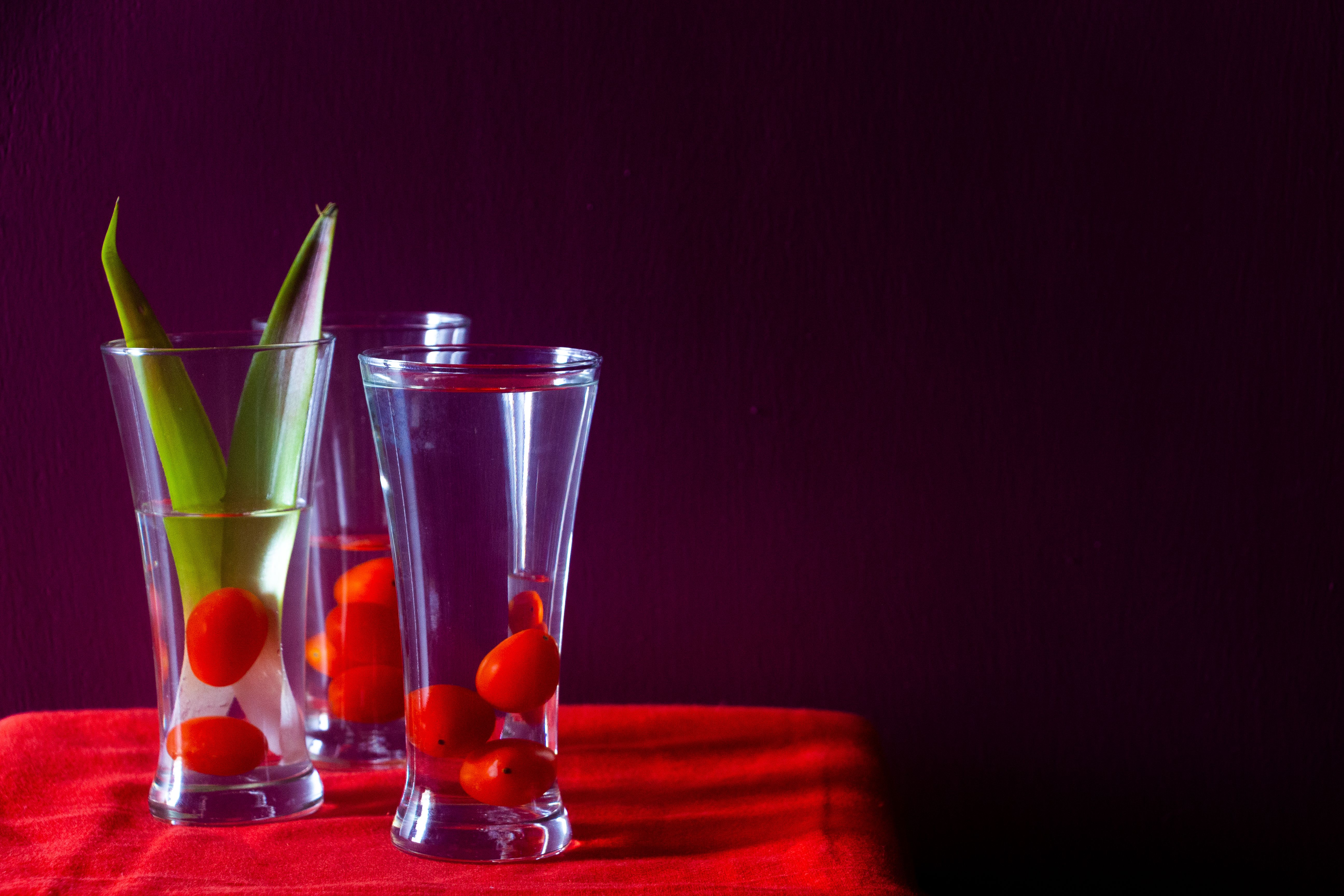 Artistic still life of cherry tomatoes in glass, featuring vibrant red and green tones.