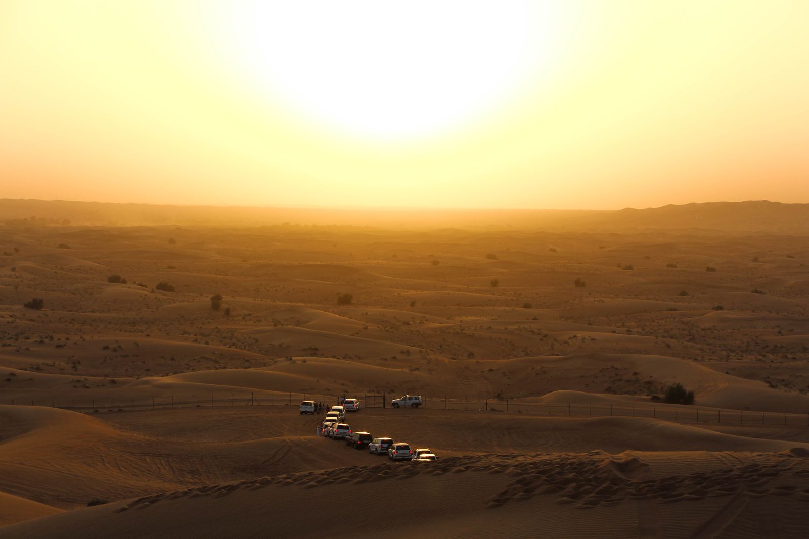 Off-road vehicles traverse the desert dunes under a warm golden sunset, ideal for adventure travel.