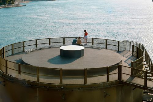 Free Two people relax on a circular pier, overlooking a calm blue sea on a sunny day. Stock Photo