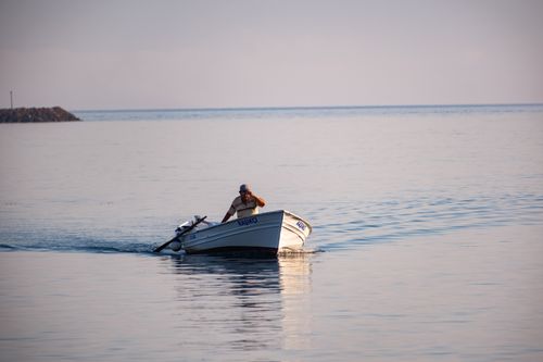 Free Tranquil scene of a fisherman in a boat on calm waters at sunset in Foça, İzmir, Türkiye. Stock Photo