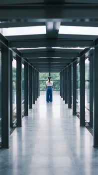 A modern glass corridor indoors featuring a single person walking away, creating a sense of perspective.