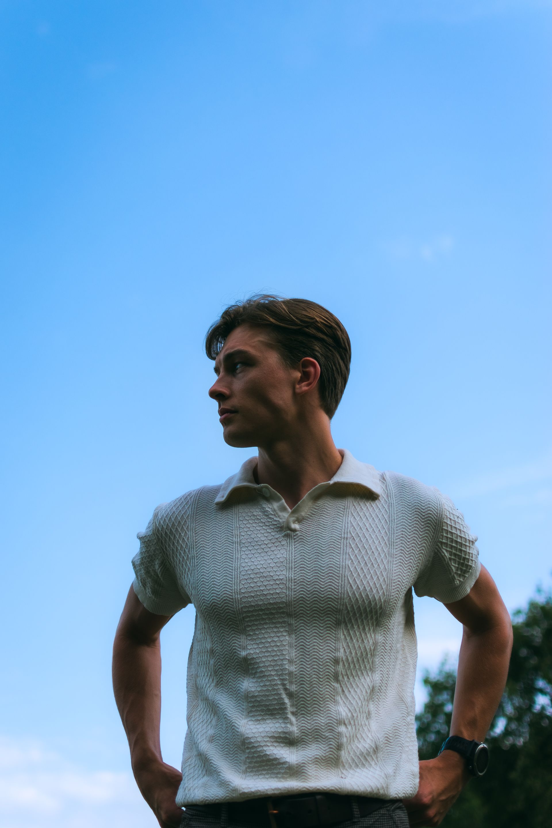 A fashionable young man poses confidently under a clear blue sky, showcasing summer style.