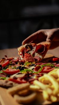 Close-up of a hand grabbing a slice of pepperoni pizza with fresh toppings. Perfect for food lovers.