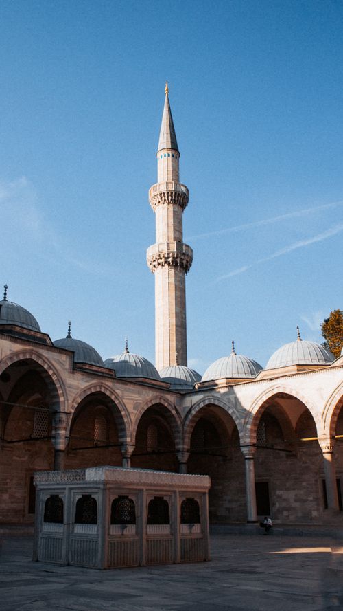 Free Serene view of an Ottoman mosque courtyard with a tall minaret under clear blue skies, capturing its architectural grandeur. Stock Photo