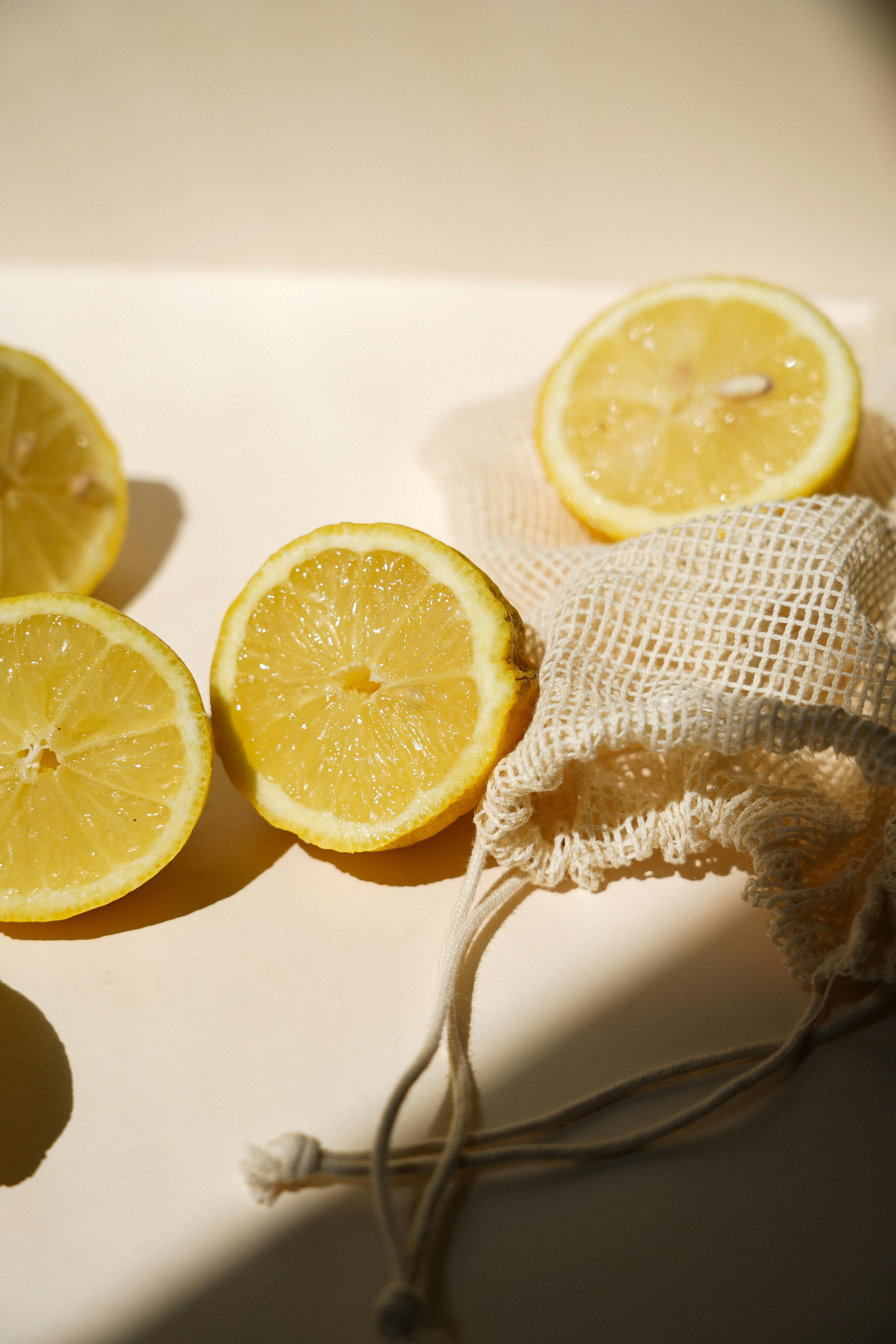 Slices of fresh lemons with a mesh bag on a sunny surface, highlighting their juicy texture.