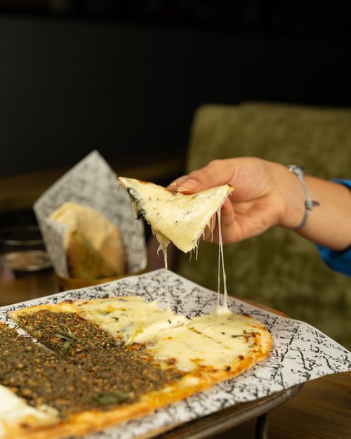 Free A close-up of a hand pulling a cheesy slice from a Turkish pide, showcasing its appetizing texture. Stock Photo