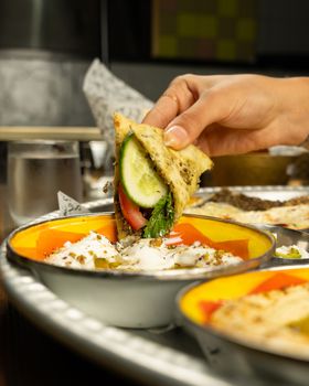Close-up of a hand dipping stuffed flatbread into a creamy sauce, perfect for food lovers.