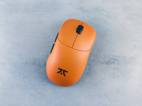 Orange computer mouse on a textured gray surface, showcased simply and artistically.