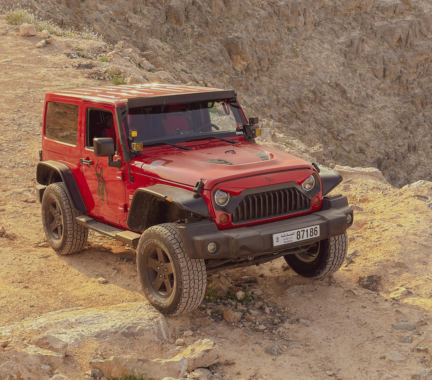 A red SUV navigates rugged terrain in Ras Al-Khaimah, UAE, demonstrating off-road capabilities.