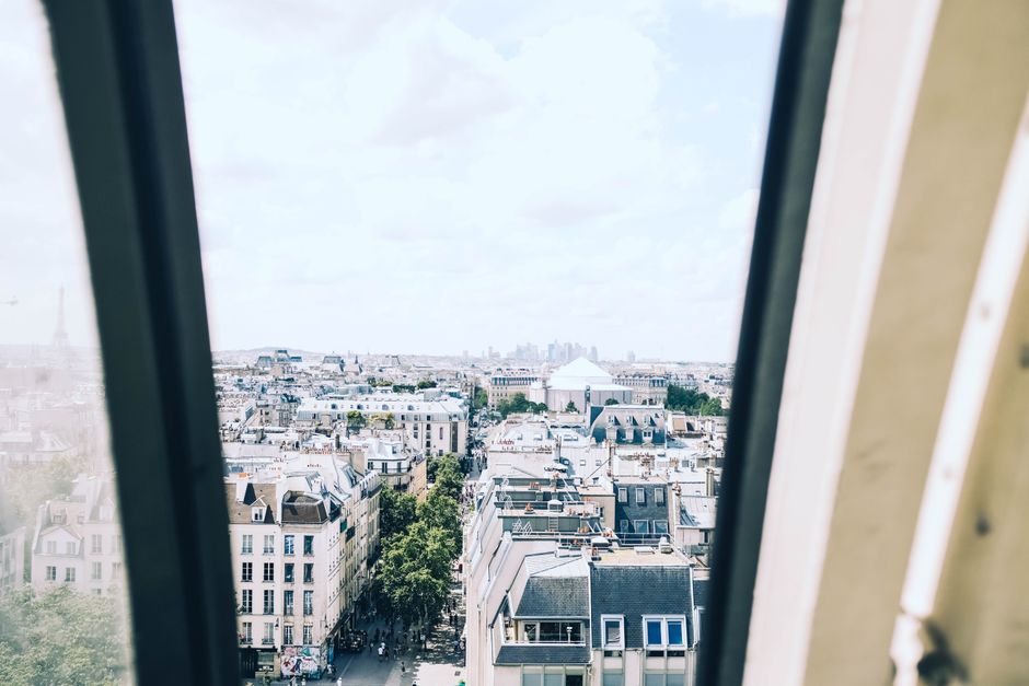 A high-angle view over the rooftops of Paris, showcasing the city's historic architecture with the Eiffel Tower in the distance.