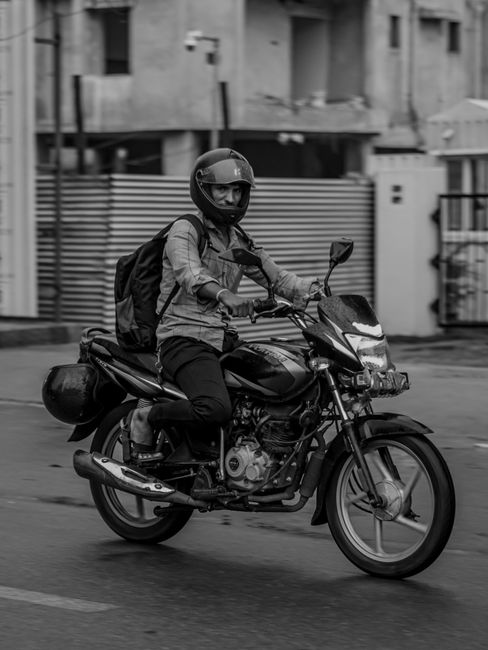 Black and white photo of a motorcyclist with helmet and backpack in Bhubaneswar, India.