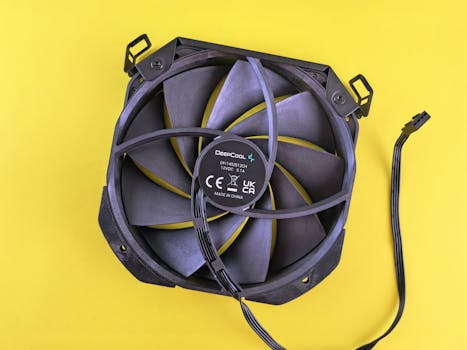 Black computer cooling fan with wire on vibrant yellow background. Ideal for technology content.