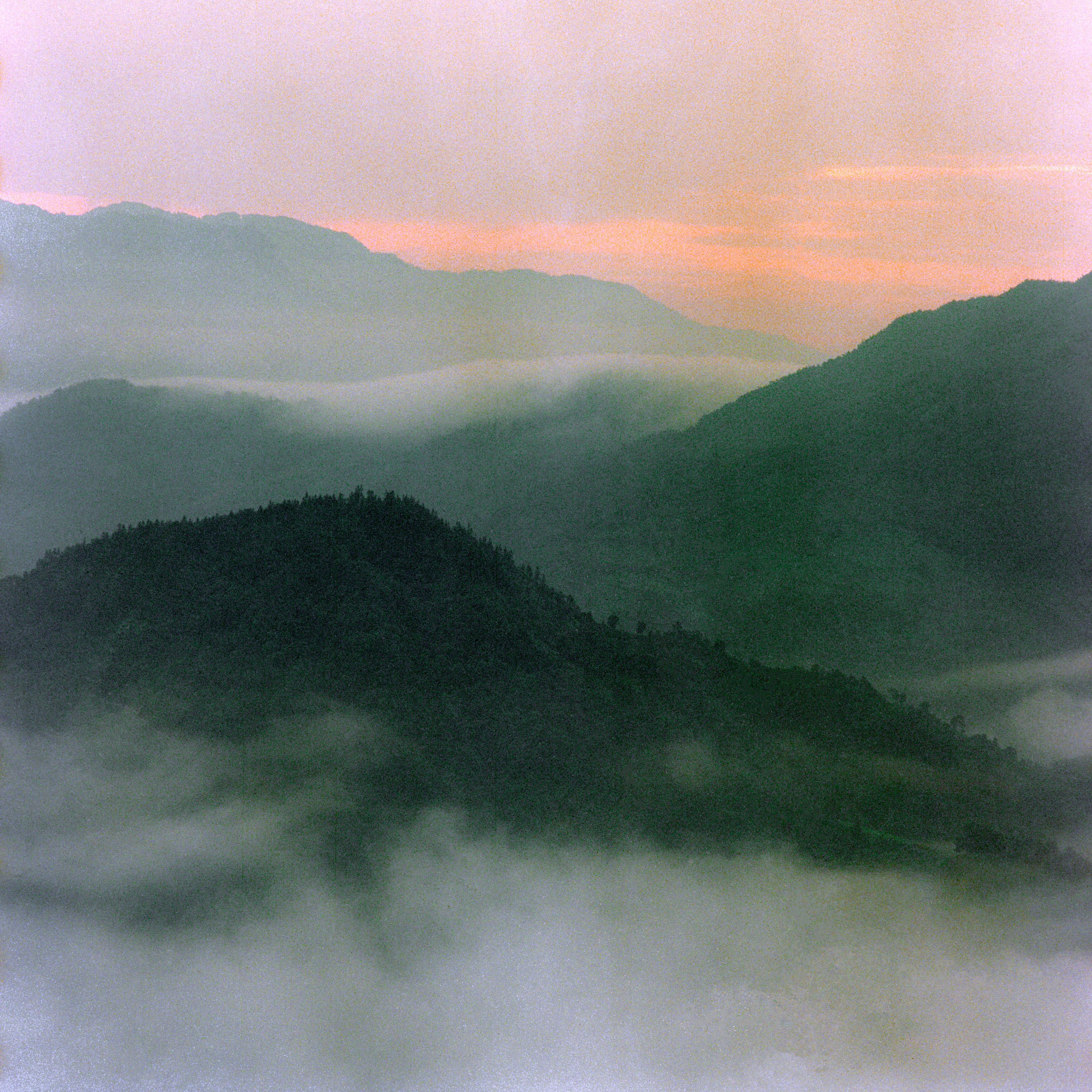 a sunset over mountains with fog and clouds