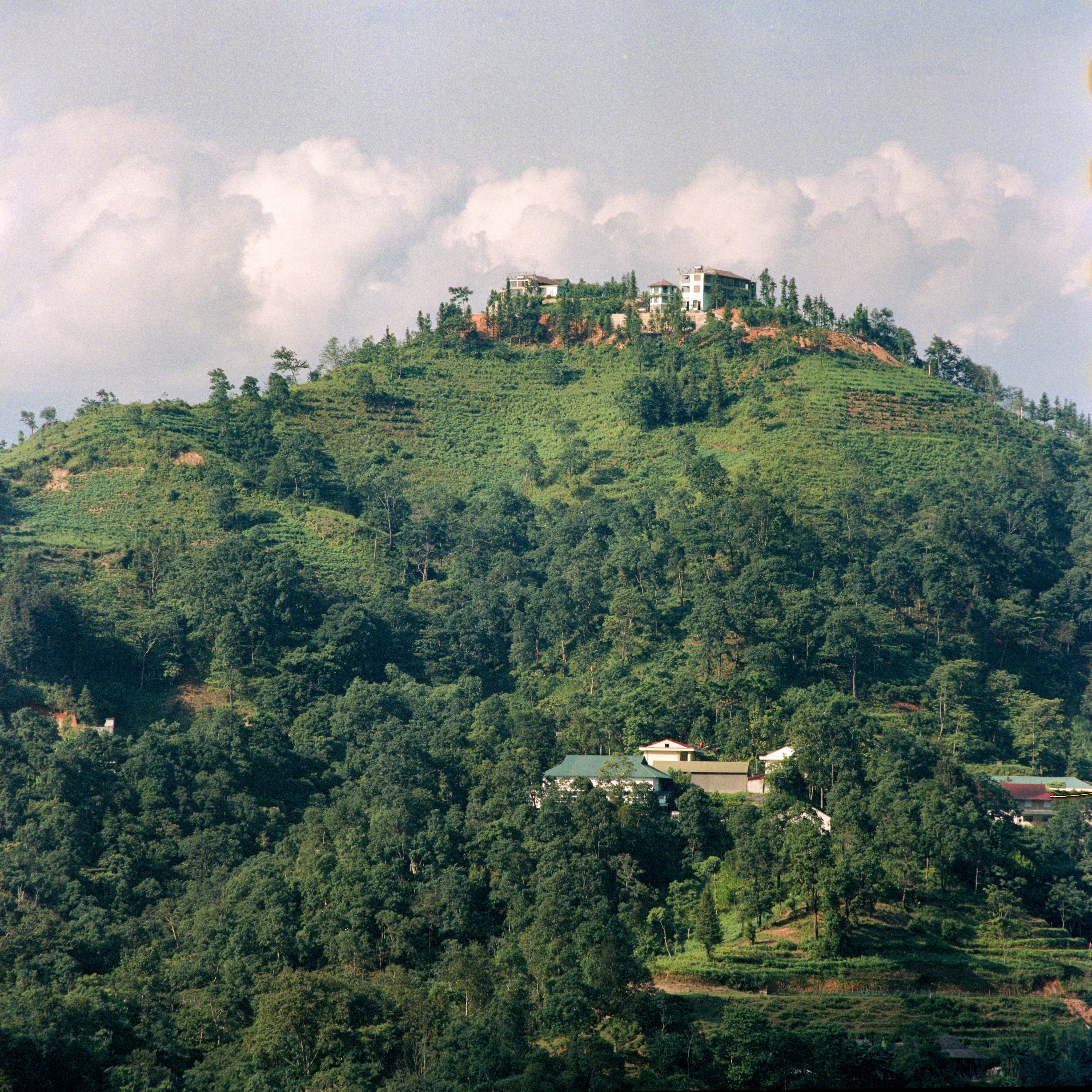 Lush green hills with houses atop, under a clear summer sky in Hà Giang, Vietnam.