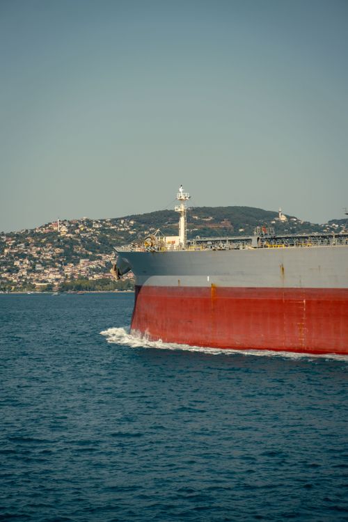 Free Front view of a large cargo ship sailing near a coastal landscape under clear sky. Stock Photo