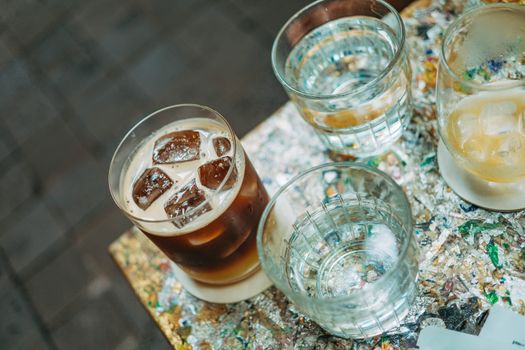 A variety of chilled beverages with ice on a colorful, textured table surface.