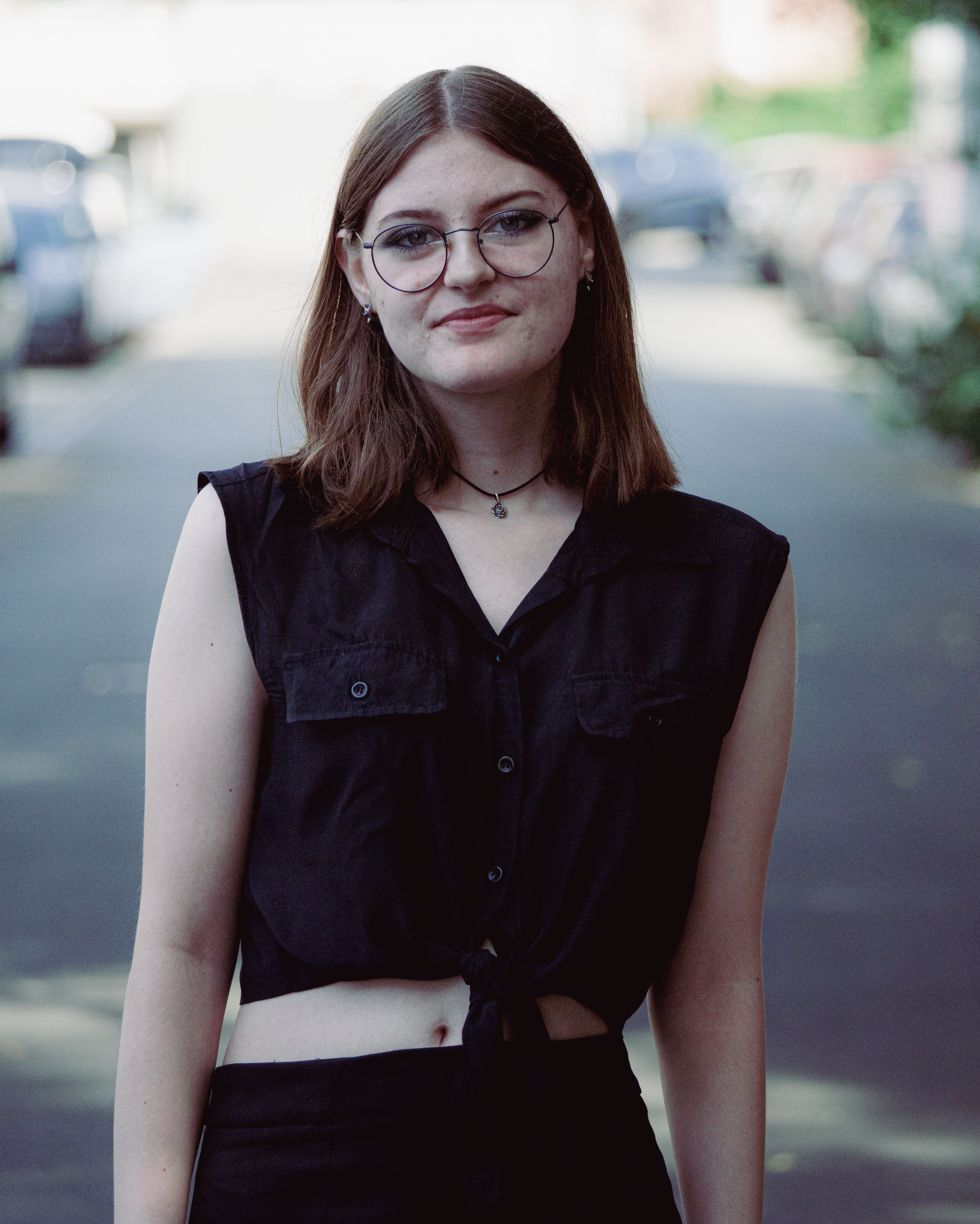 Chic urban fashion portrait featuring a woman with glasses wearing a black vest on city streets.