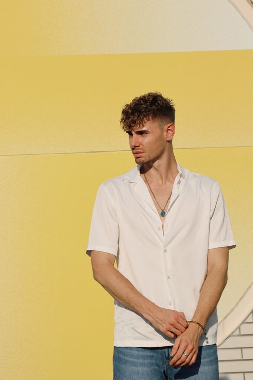 Free Stylish young man stands pensively in Berlin, wearing casual fashion against a vibrant yellow wall. Stock Photo