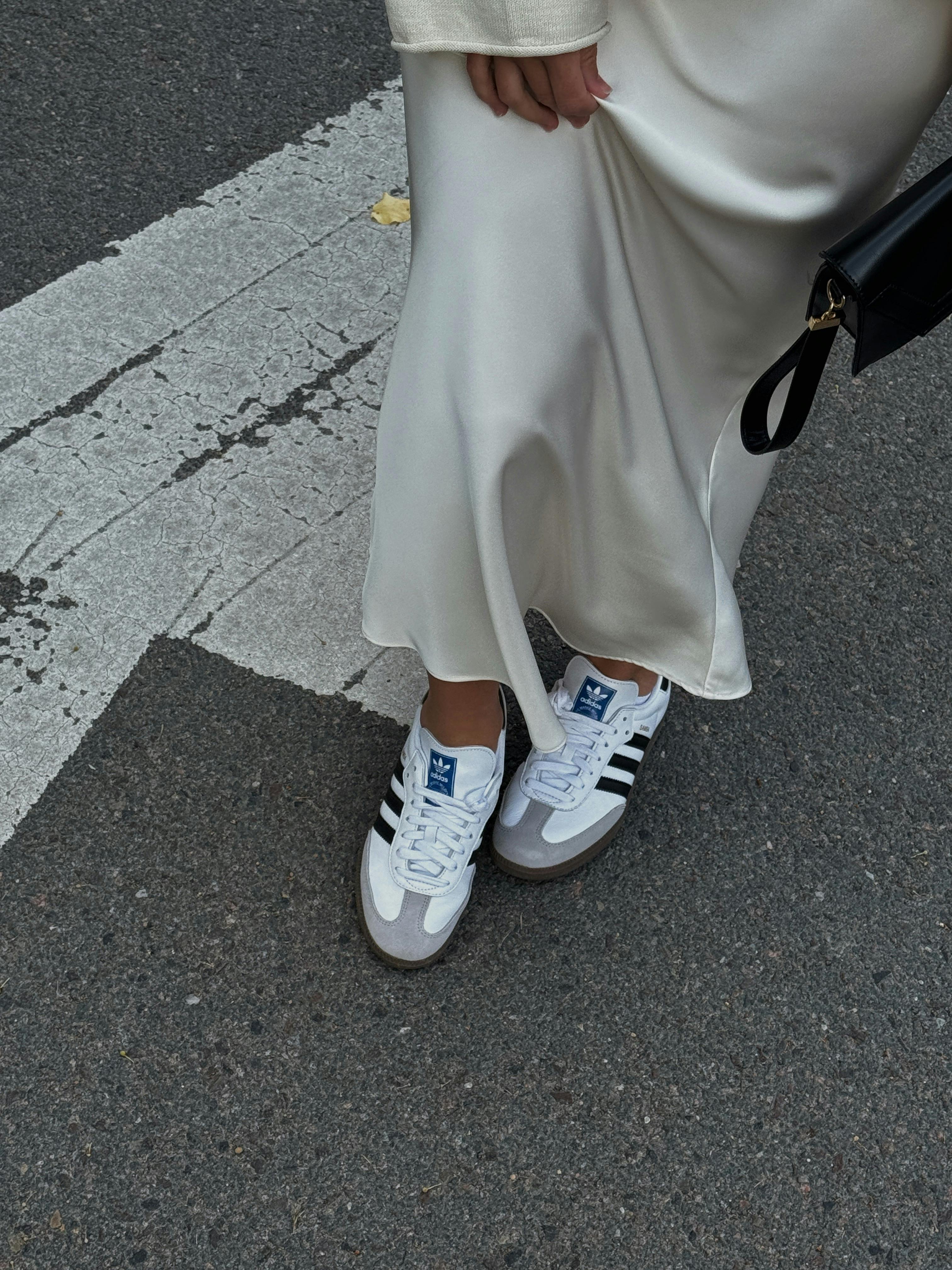 White satin dress paired with stylish sneakers on a city street.