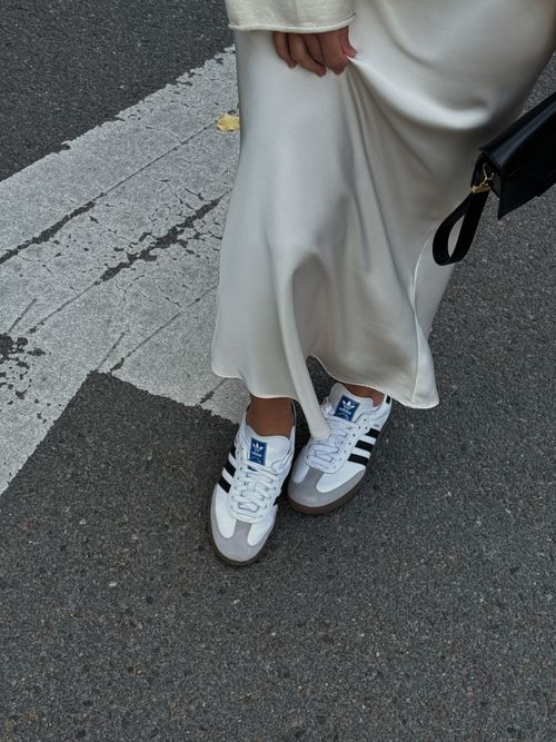 Free White satin dress paired with stylish sneakers on a city street. Stock Photo