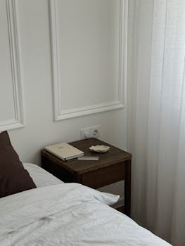 Minimalist bedroom corner with white walls, brown nightstand, and simple accessories.